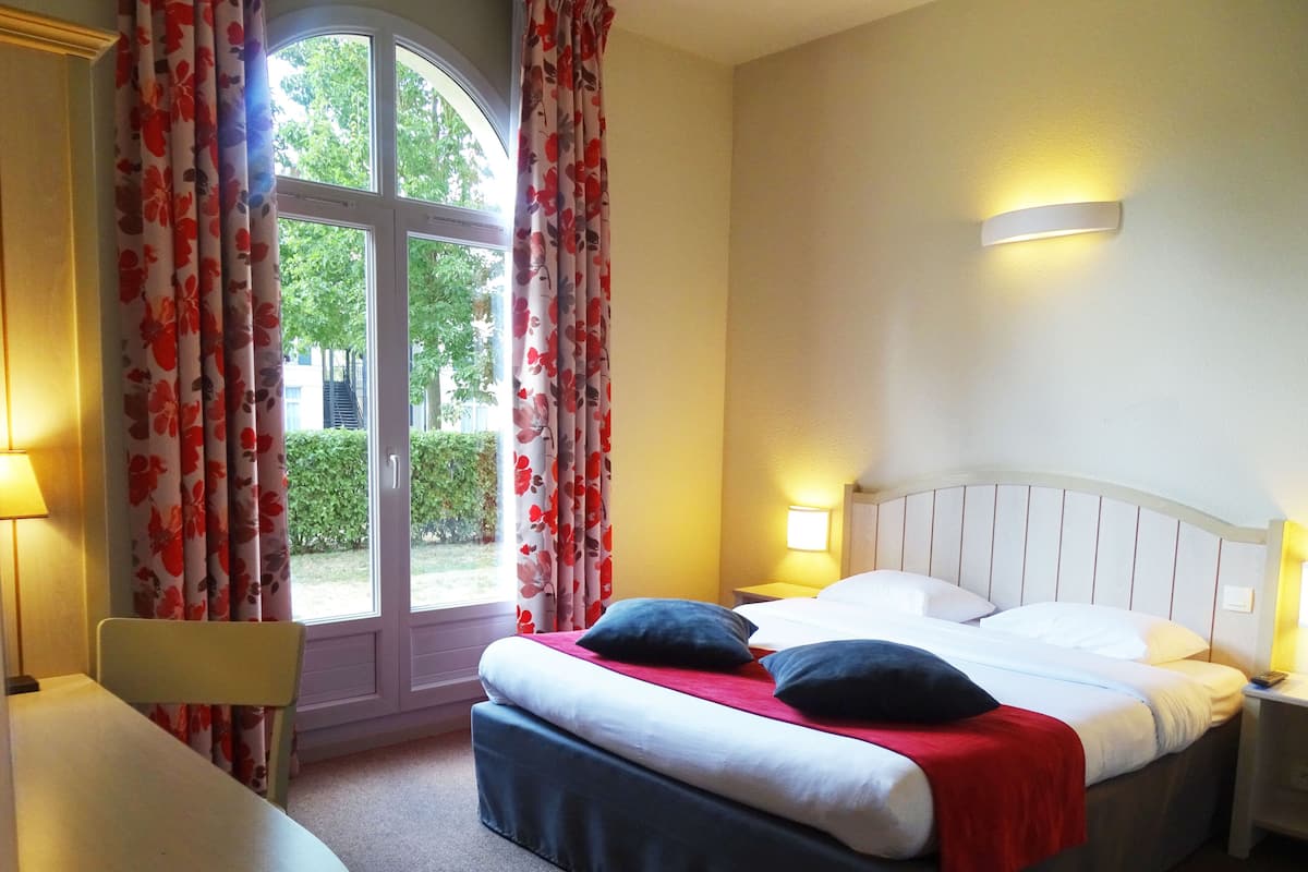 A hotel room with a bed, two bedside tables with lamps, a chair, and a window with curtains.