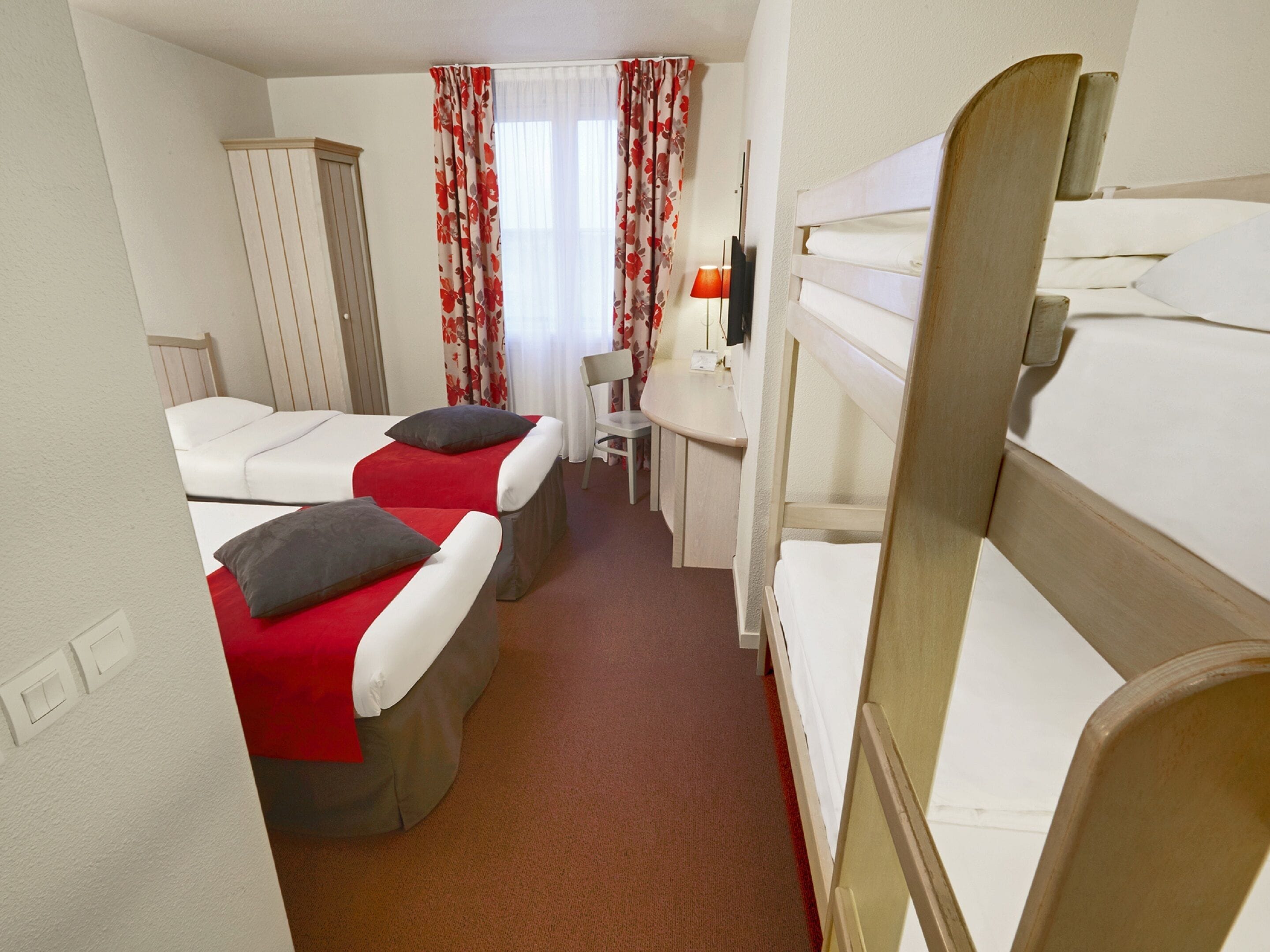 A hotel room with two beds, a desk, a chair, and a TV.