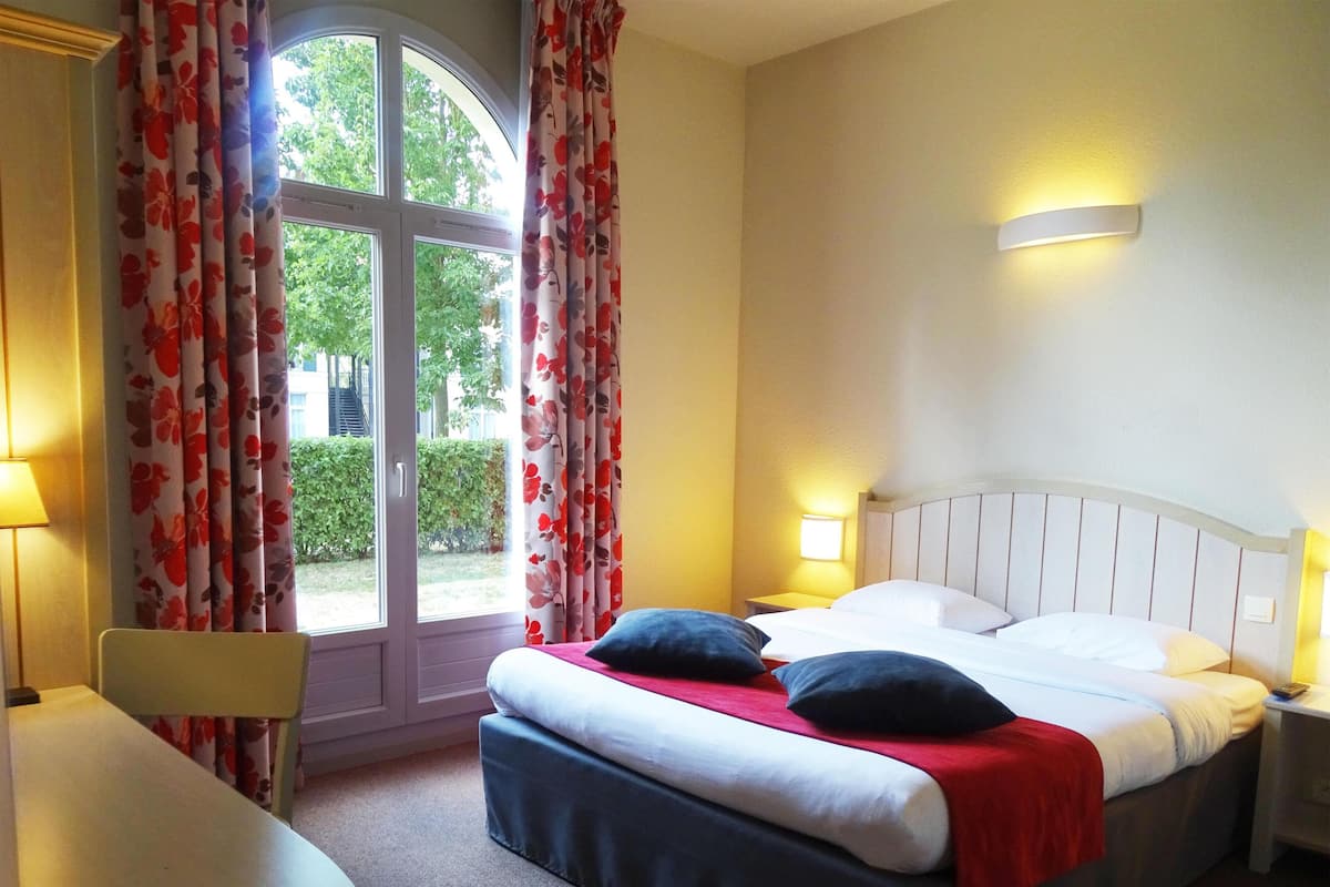 A hotel room with a bed, two bedside tables with lamps, a chair, and a window with curtains.