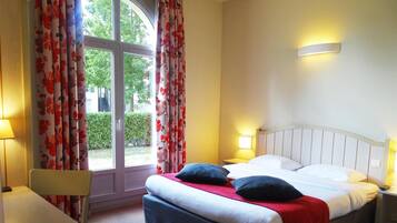 A hotel room with a bed, two bedside tables with lamps, a chair, and a window with curtains.