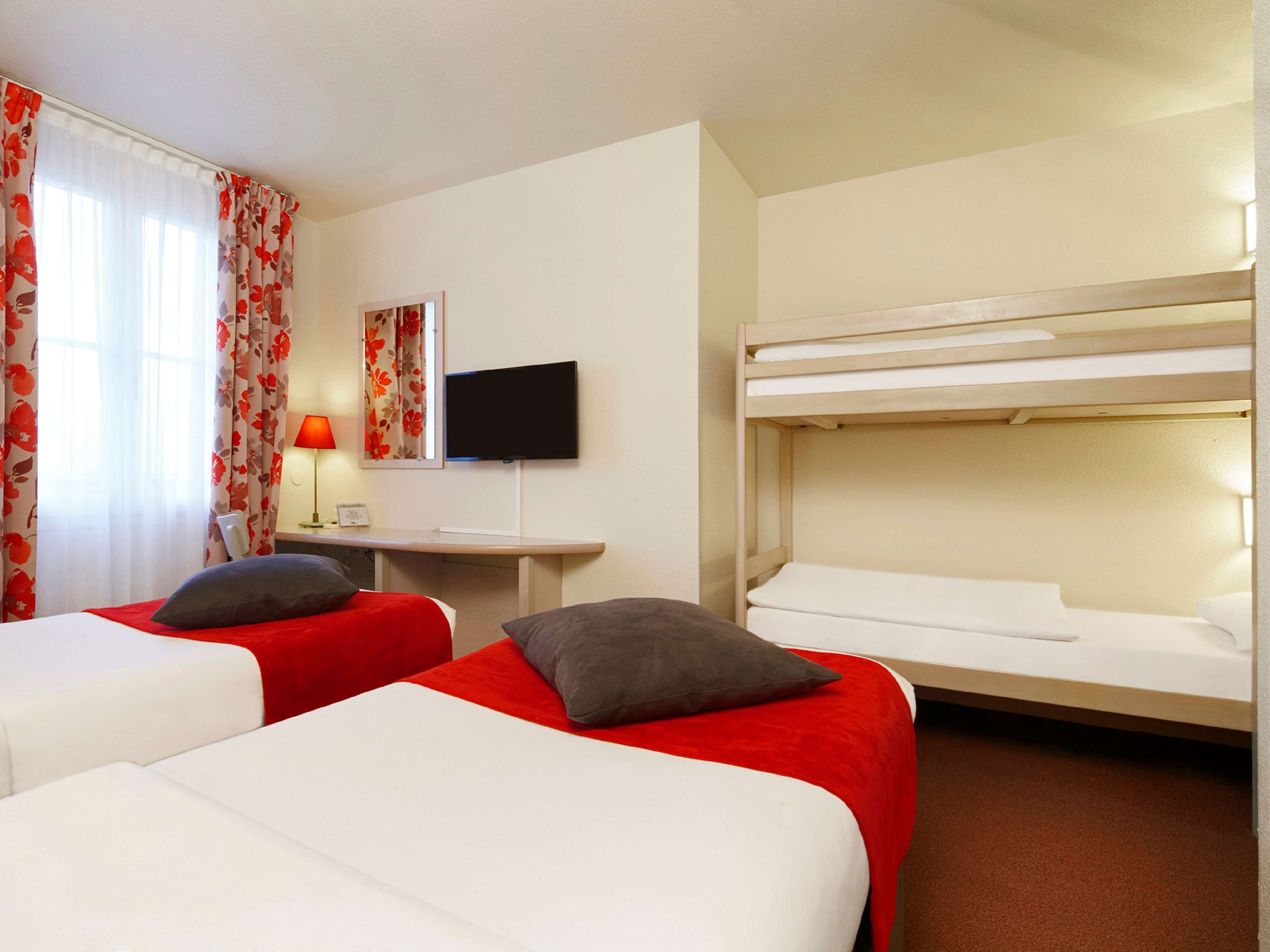 A hotel room with two beds, a desk, a television, and a window with curtains.