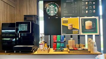 A Starbucks coffee shop interior with a menu board, coffee machines, and a display of branded merchandise.