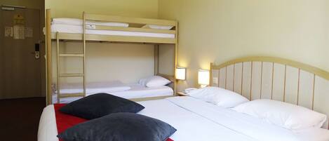 Una habitación de hotel con una cama litera, una cama individual con una colcha roja y dos lámparas de noche.