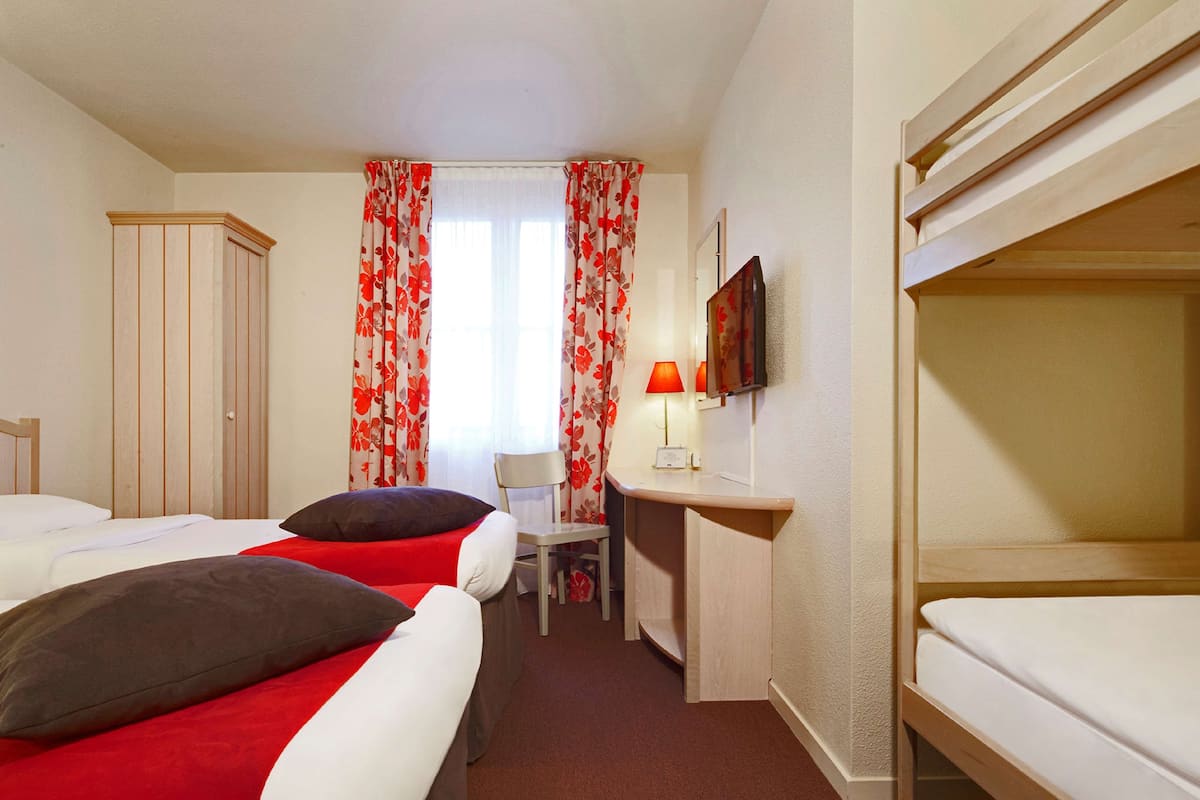 A hotel room with two beds, a desk, a chair, a television, and a wardrobe.