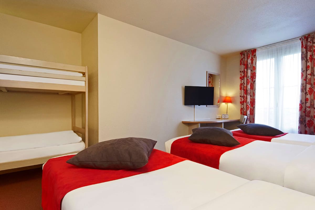 A hotel room with two single beds, a bunk bed, a desk with a flat-screen TV, and a window with curtains.