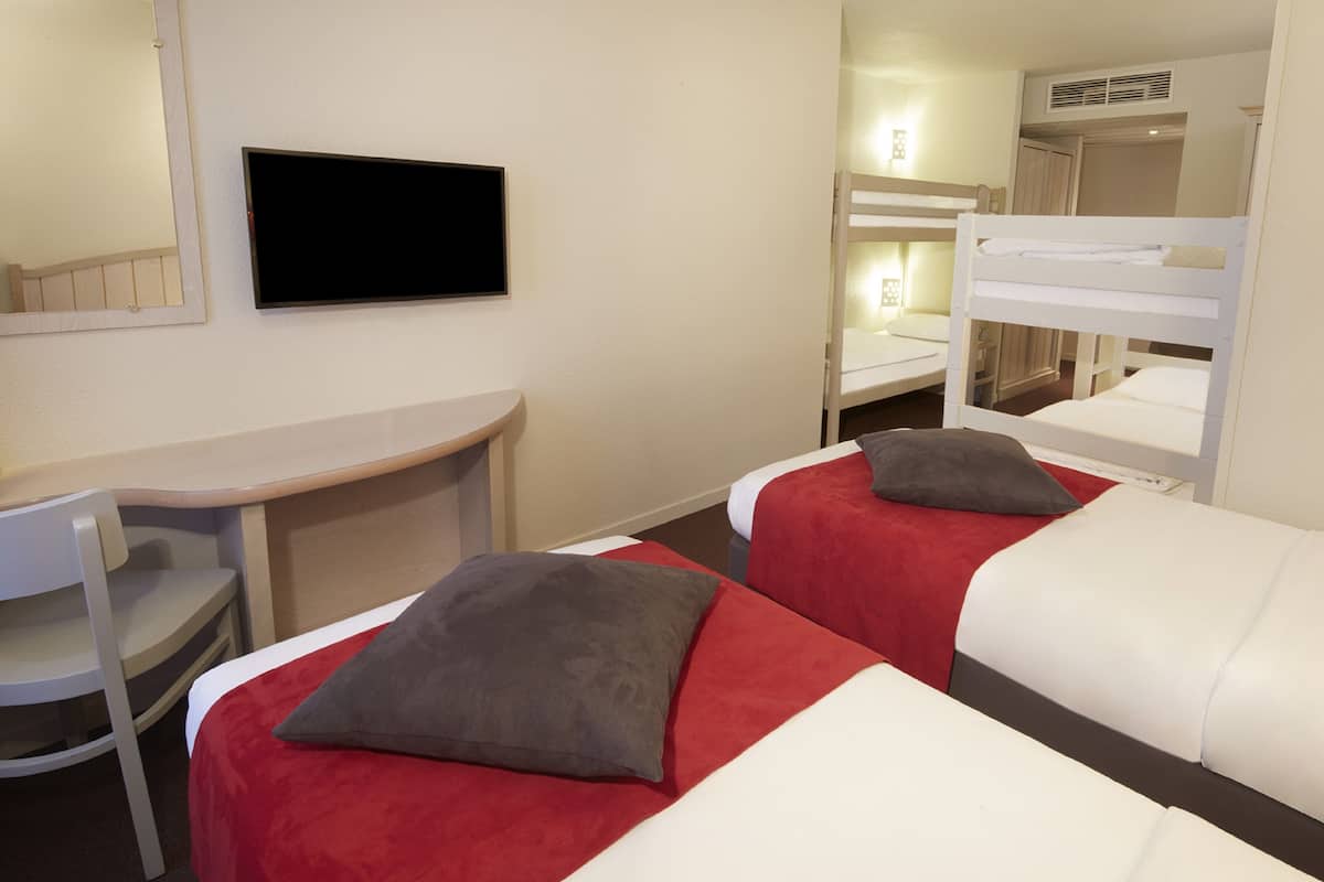 A hotel room with two beds, a desk, a chair, and a television.