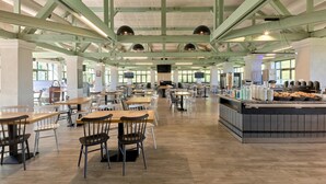 Una cafetería amplia con techos altos, gran cantidad de asientos y una zona central de servicio de alimentos.