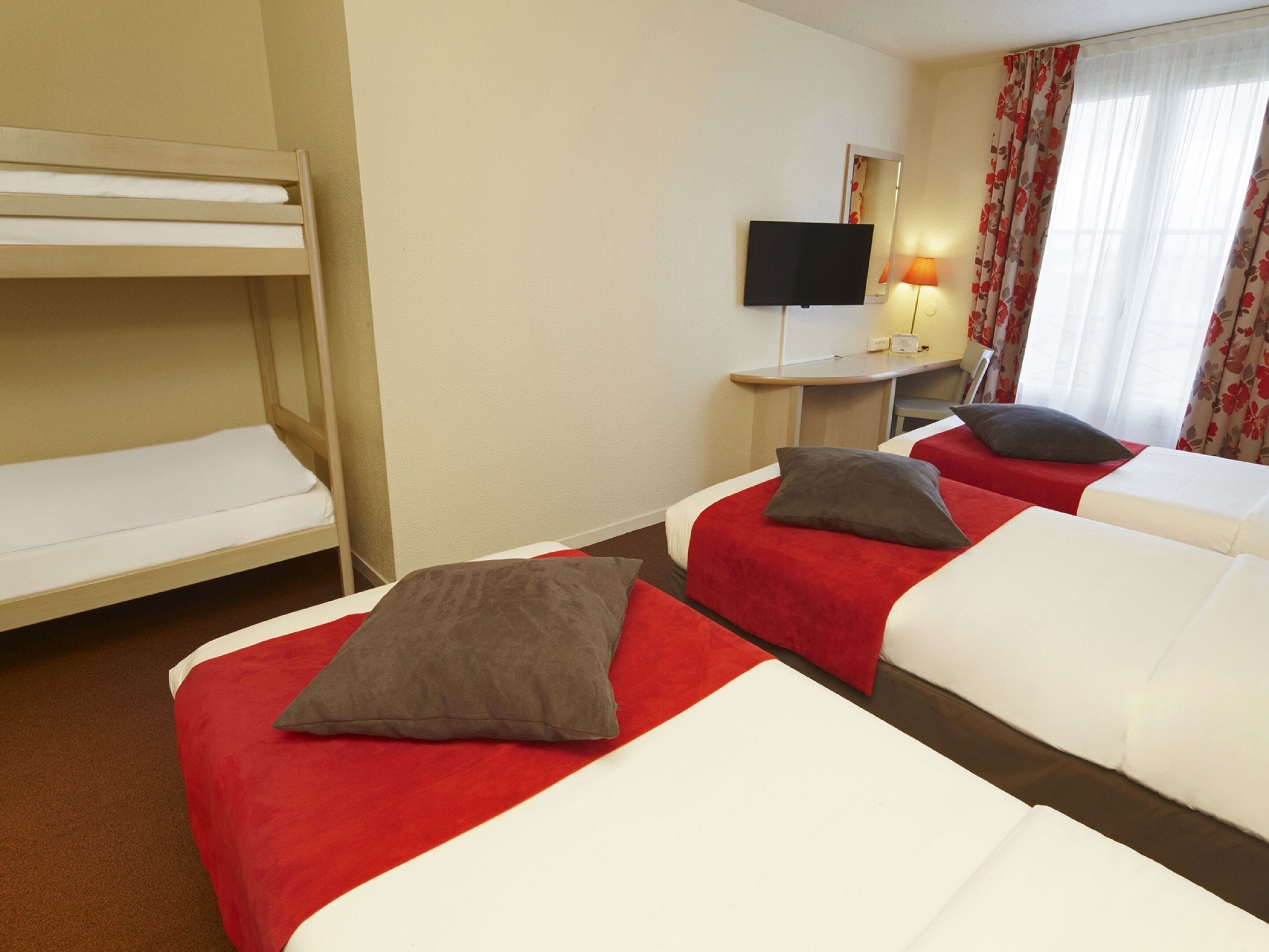 A hotel room with two single beds, a bunk bed, a desk with a television, and a window with curtains.