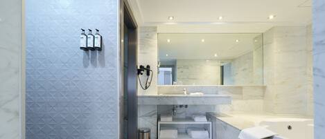 Un baño moderno con pared de mármol, un espejo grande, una bañera y un mueble de tocador con lavabo y toallero.