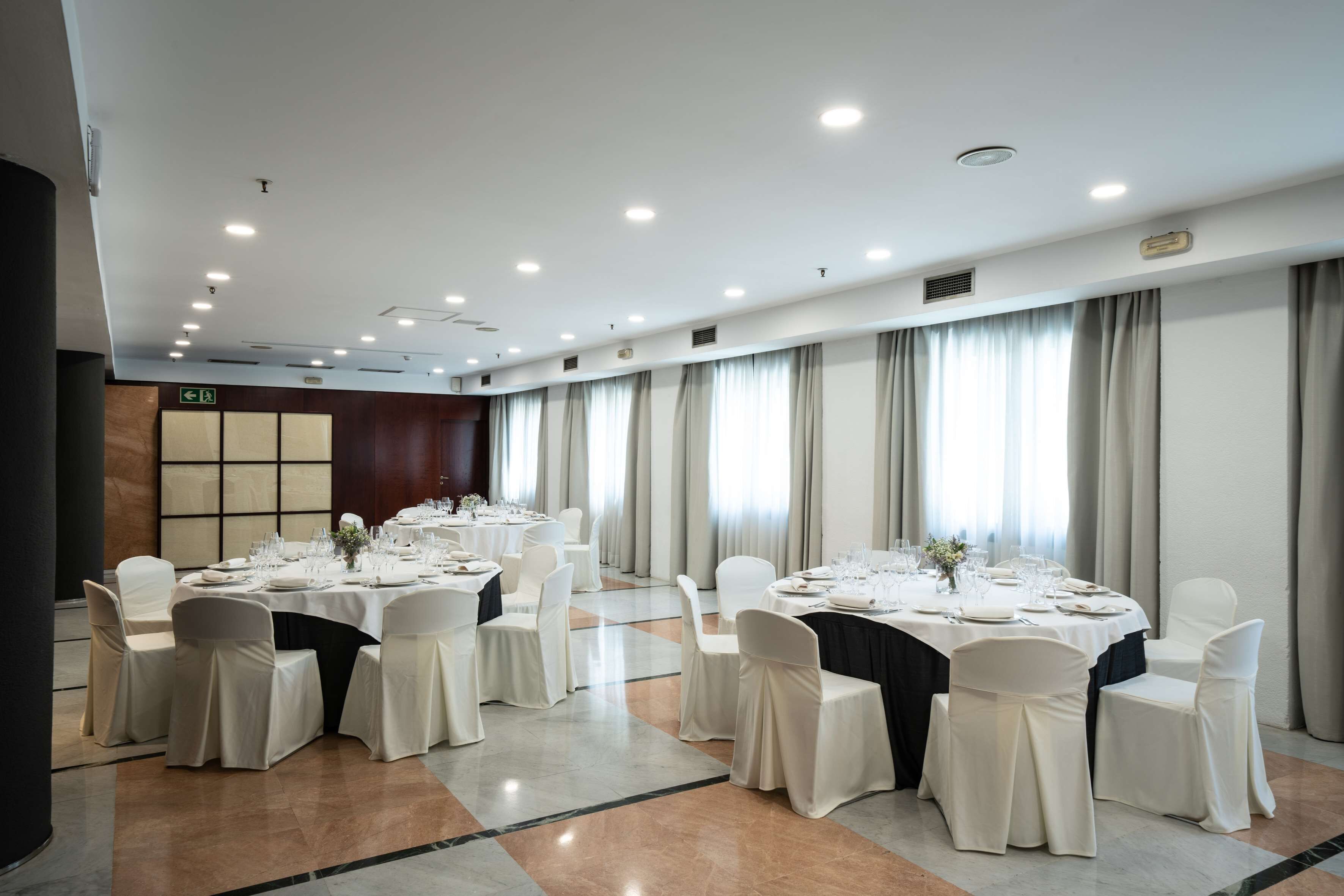 Un salón de conferencias con mesas redondas, sillas blancas y piso pulido.