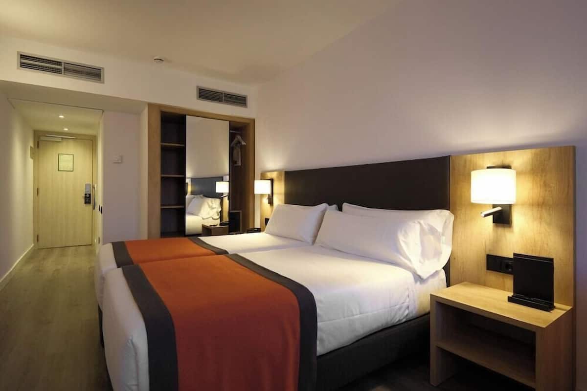 A hotel room with a bed, bedside tables, lamps, and a wardrobe.
