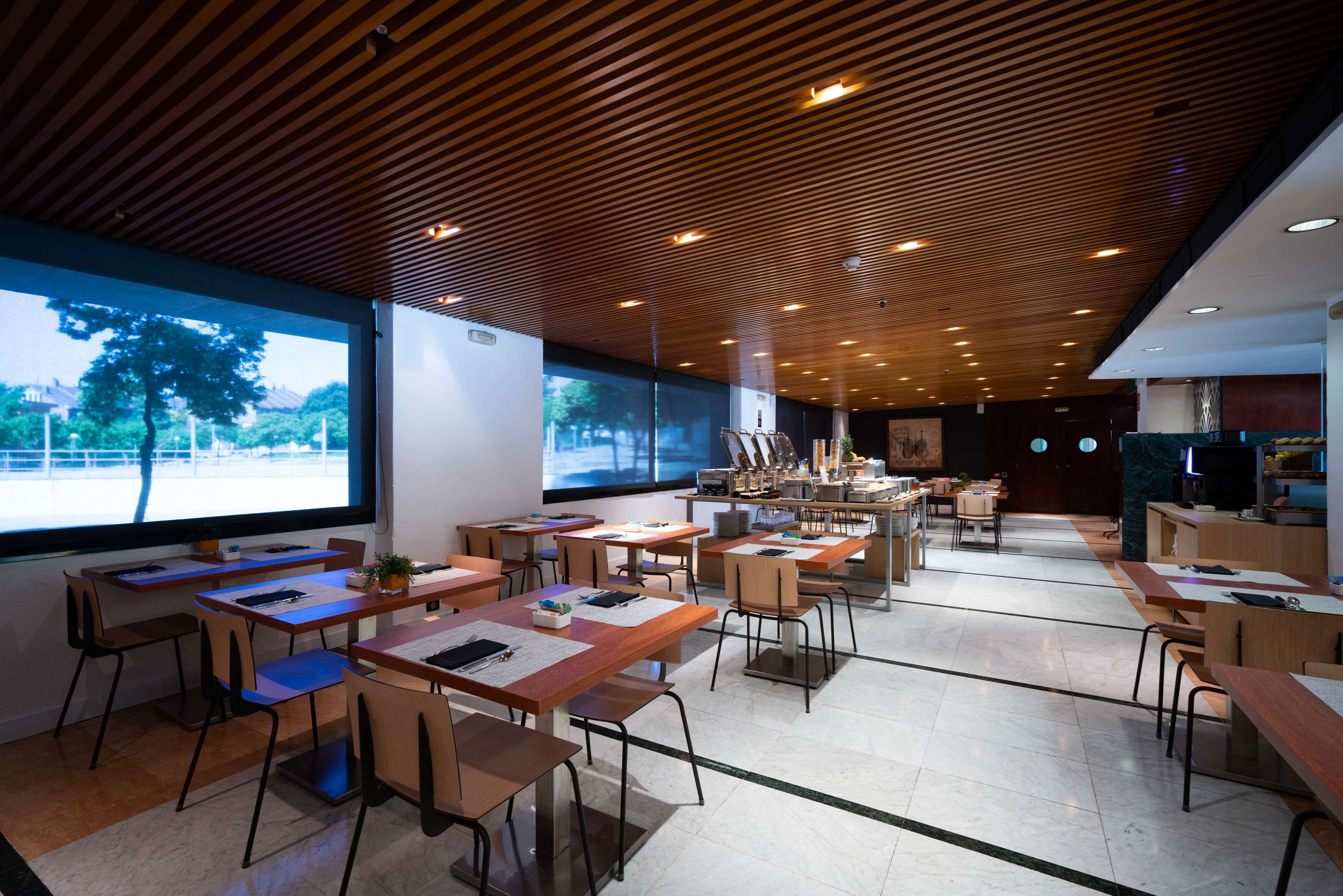 Une salle de conférence moderne, dotée de tables et de chaises en bois, de grandes fenêtres et d’un écran de projection.