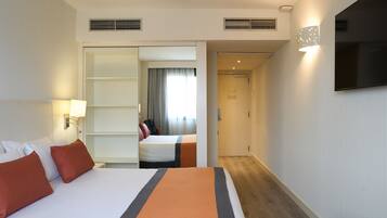 Habitación de hotel con una cama grande, un escritorio, una silla, un televisor y un baño visible a través de una puerta abierta.