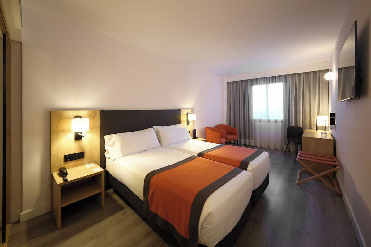A hotel room with two beds, a desk, a chair, and a TV.