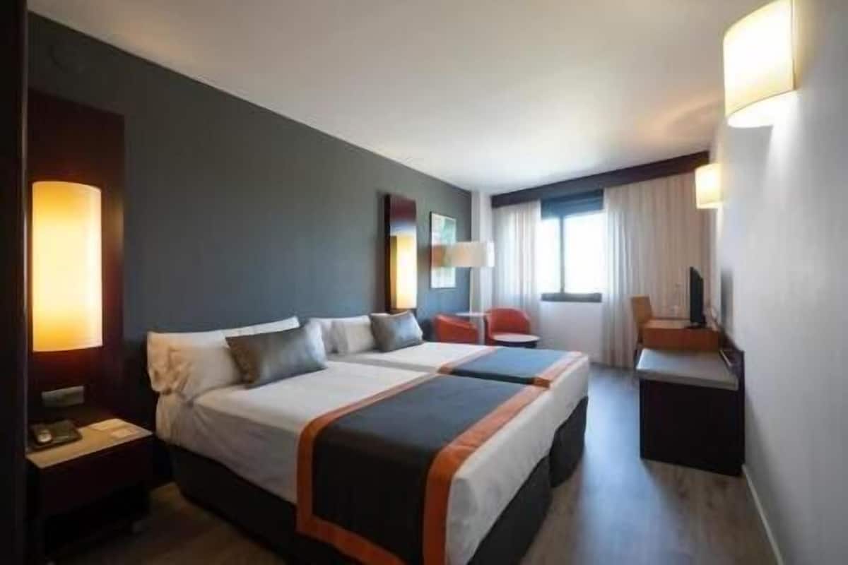 A hotel room with two beds, a desk, a chair, and a TV.