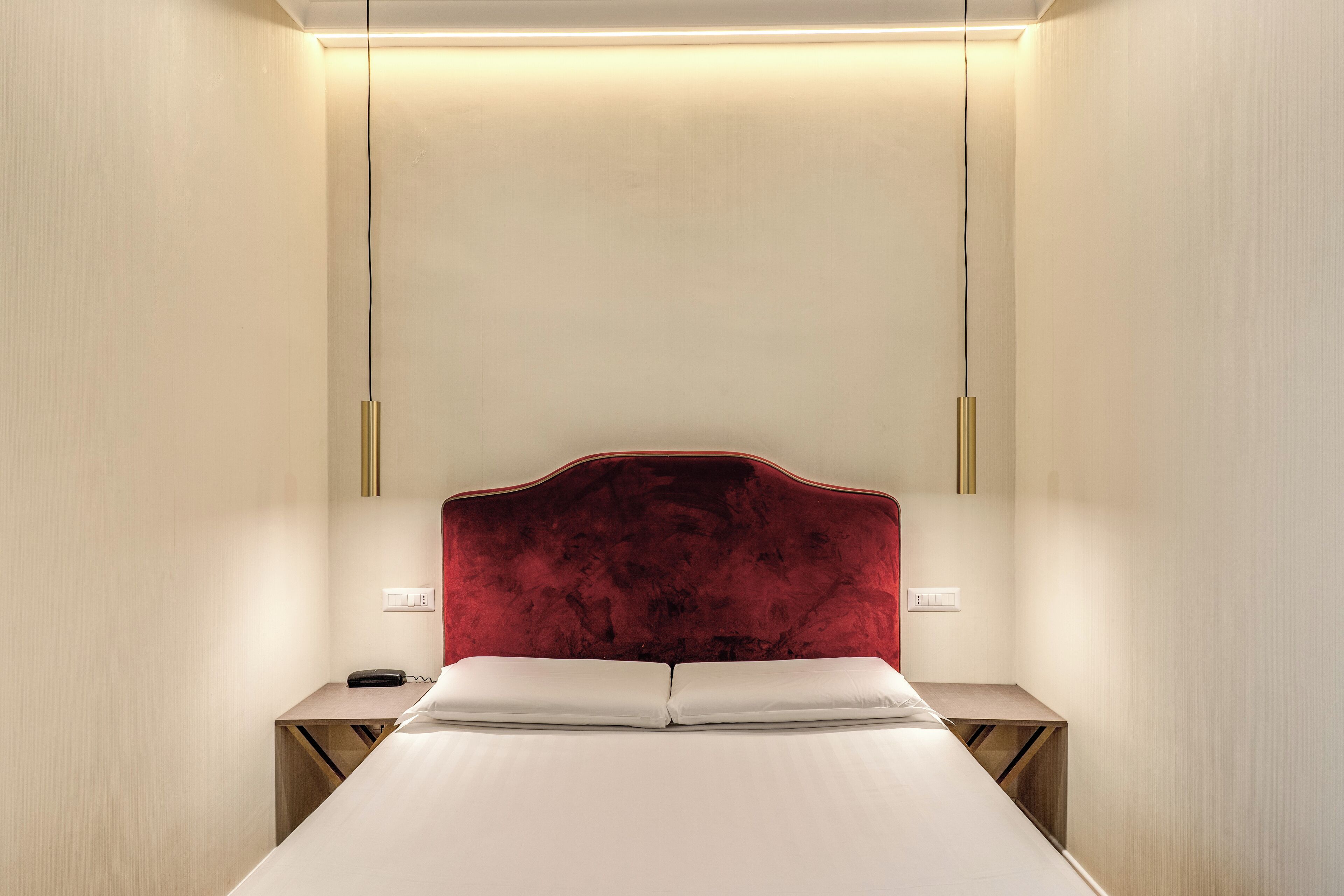 A modern hotel room with a large bed, a red headboard, bedside tables, and a phone.