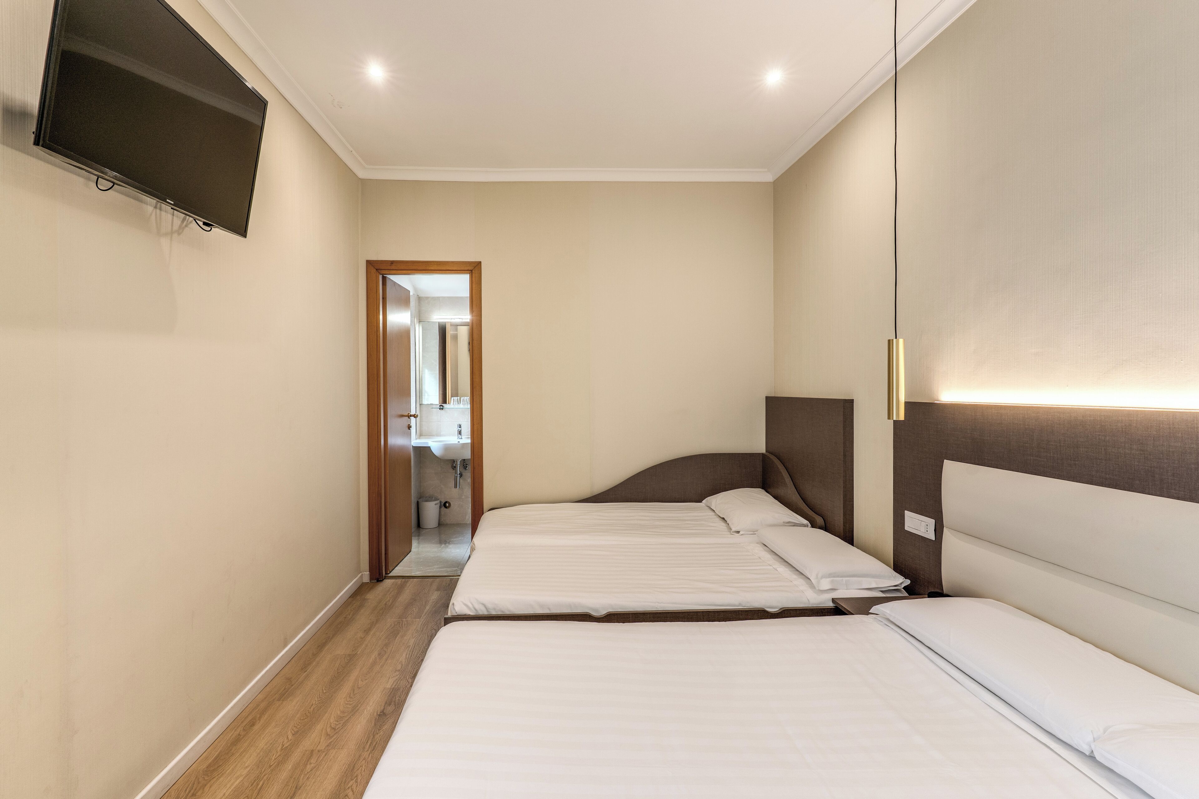 Una habitación de hotel con dos camas, un televisor montado en la pared y piso de madera.