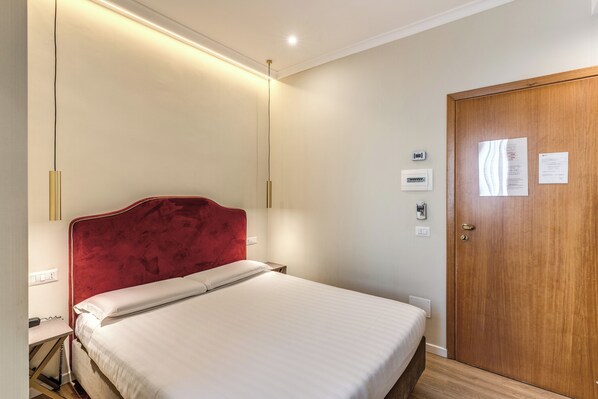 A hotel room with a bed, a wooden door, and a bedside table. - Flower Garden Hotel Rome (Rome)