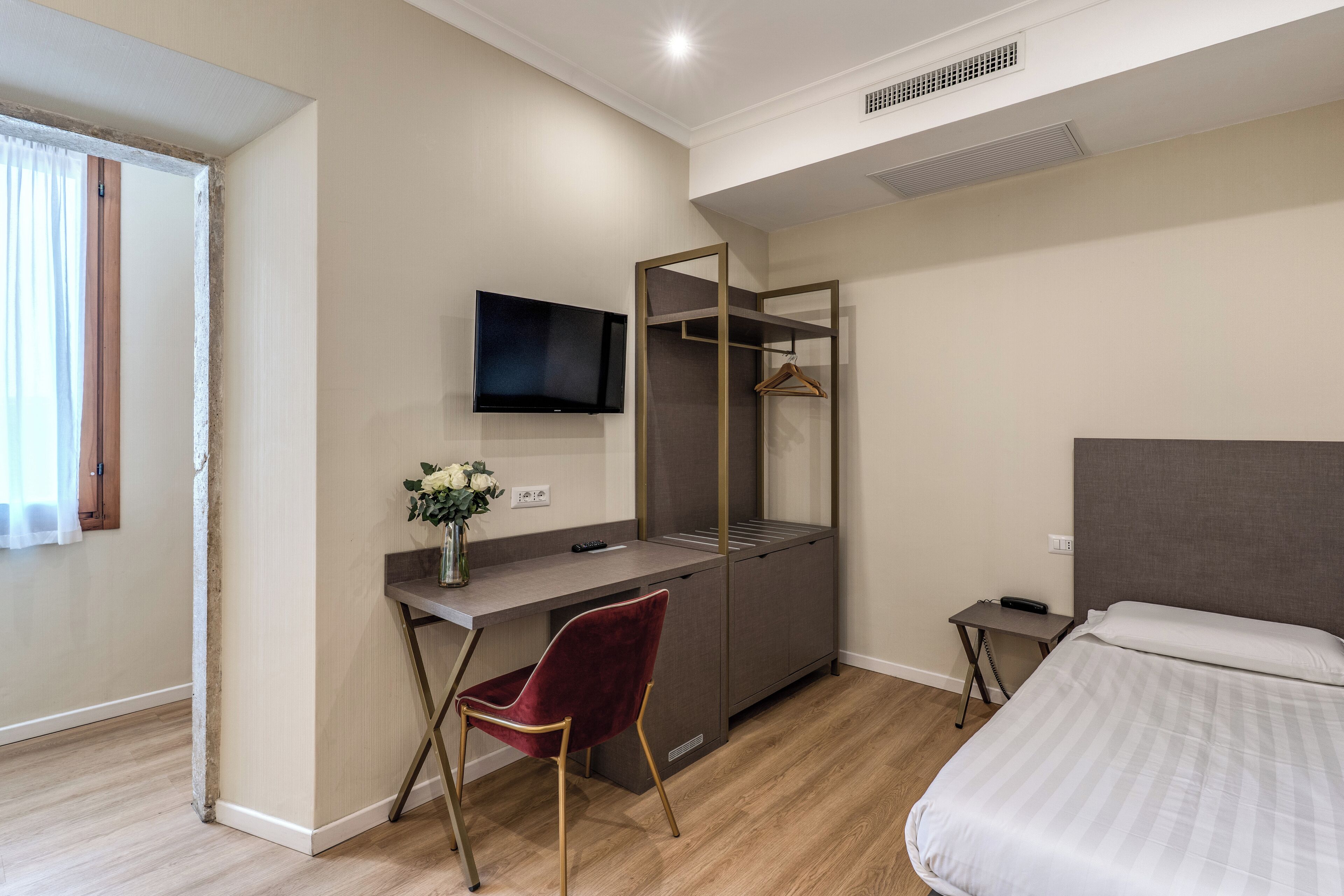 Hotelkamer met een bed, bureau met stoel, televisie aan de muur en een klein tafeltje met een afstandsbediening.