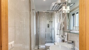 A modern bathroom with a glass-enclosed shower, a white sink, and a glass shelf with toiletries. - Flower Garden Hotel Rome (Rome)