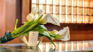 A bouquet of white tulips and lilies in a glass vase with a hotel card on a reflective surface. - Flower Garden Hotel Rome (Rome)