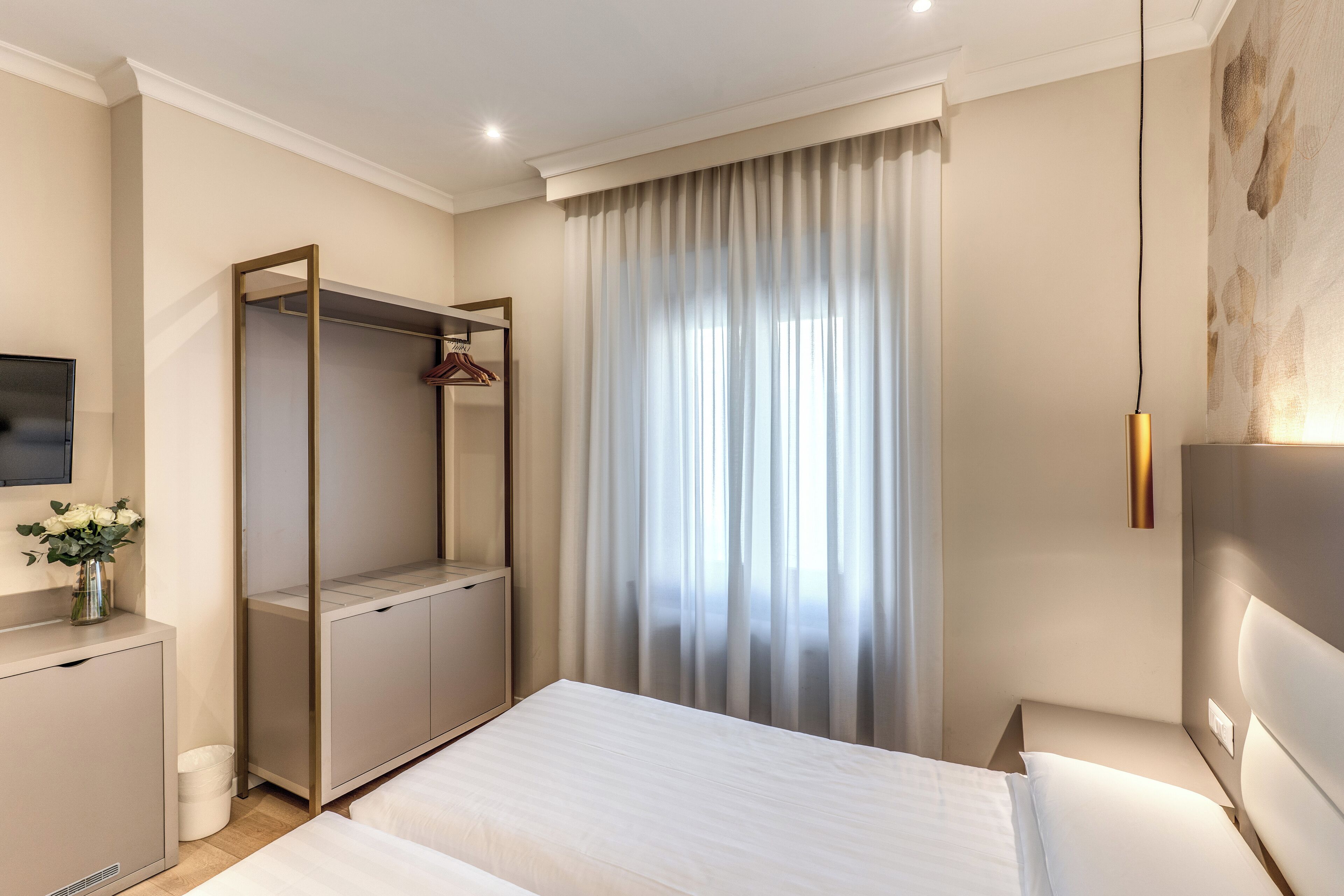 A hotel room with a bed, a wardrobe, a TV, and a window with curtains.