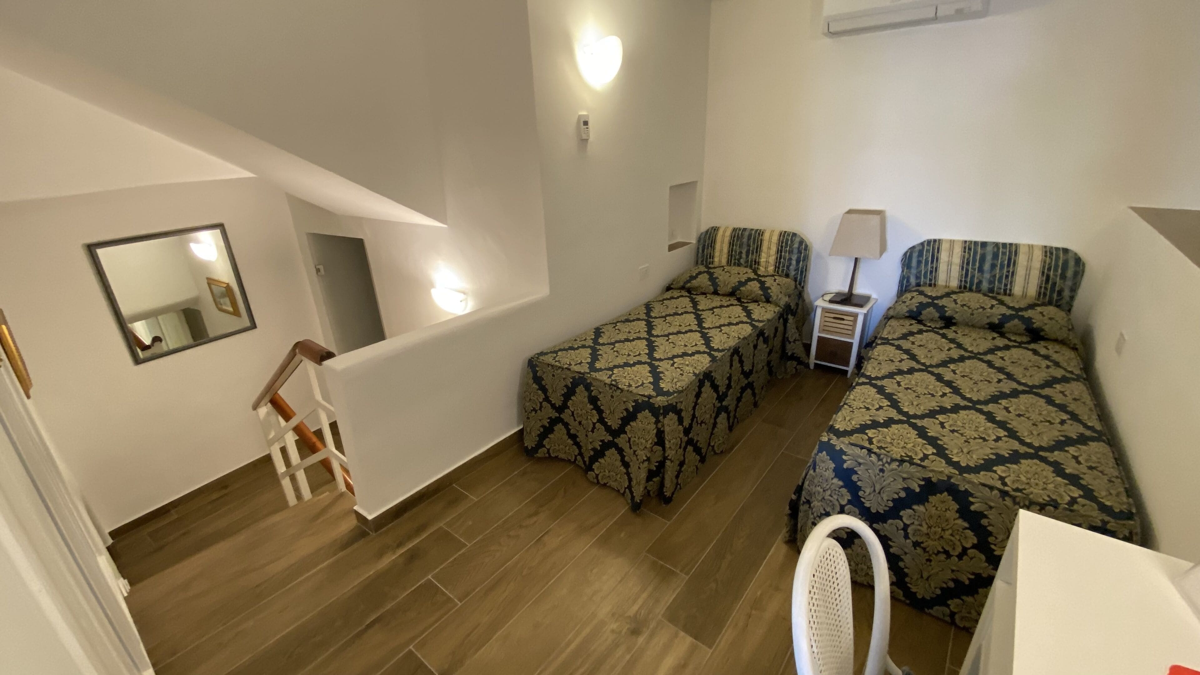 Ein Zimmer mit zwei Betten, einem kleinen Tisch, einem Stuhl, einem Spiegel und einer Treppe.
