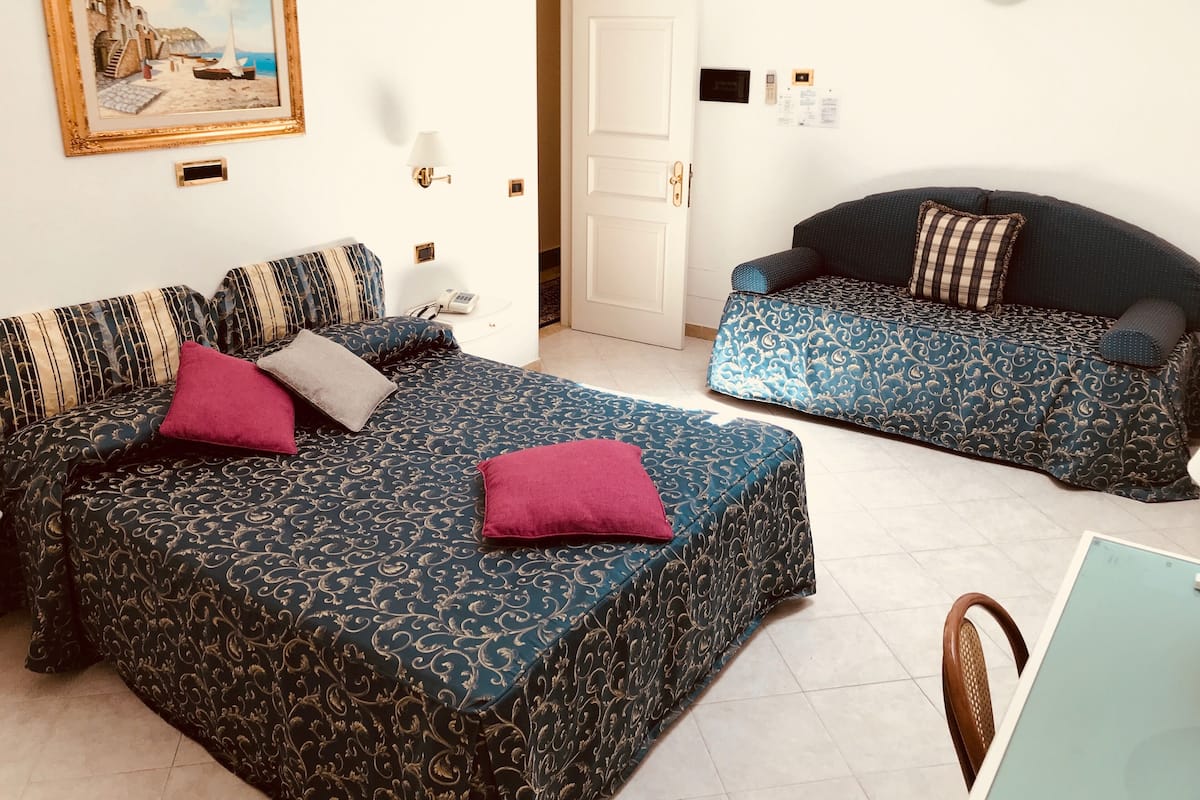 A room with a large bed, a sofa, a painting on the wall, and a door leading to another room.