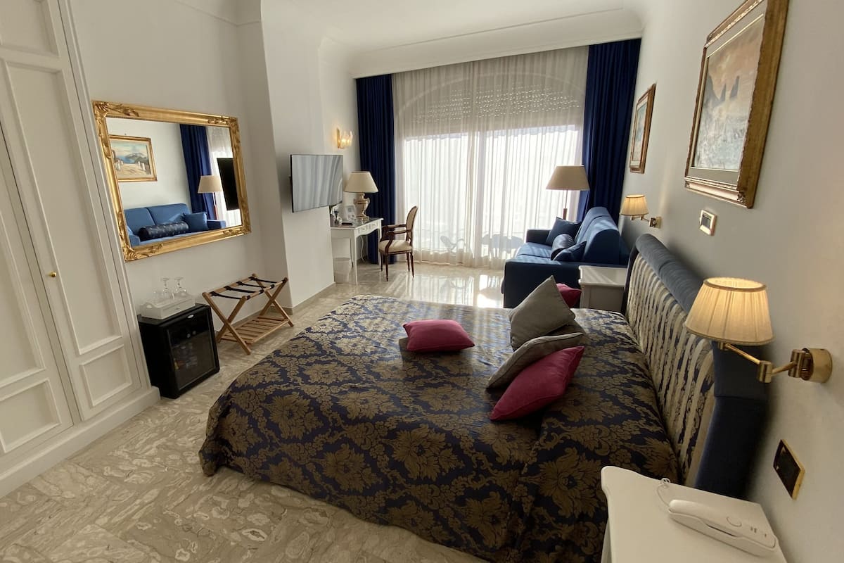 A hotel room with a large bed, a desk, a chair, a TV, and a wardrobe.