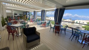 A covered outdoor seating area with tables and chairs, overlooking a residential area and the sea. - Bougainville Luxury Boutique Hotel (Anacapri)