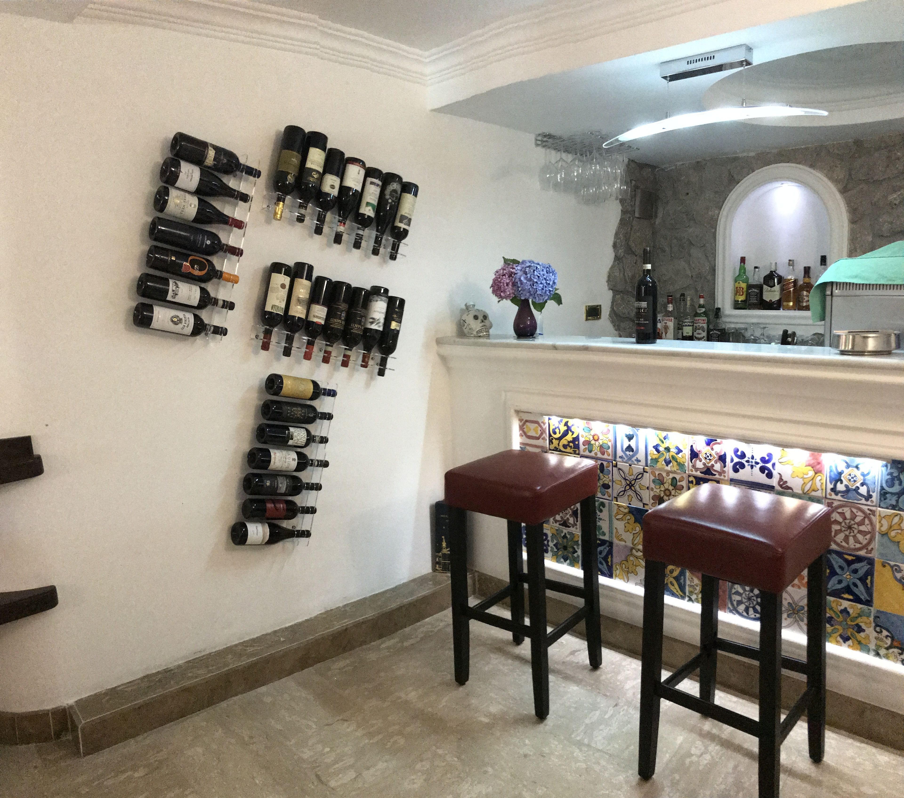 A bar area with wine bottles on the wall and two stools.