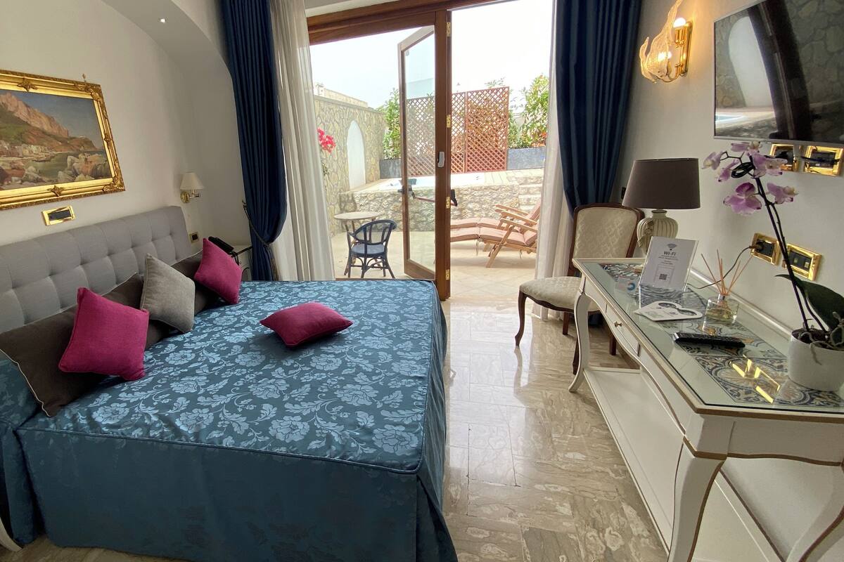 A bedroom with a bed, a desk, a chair, and a view of the outside.