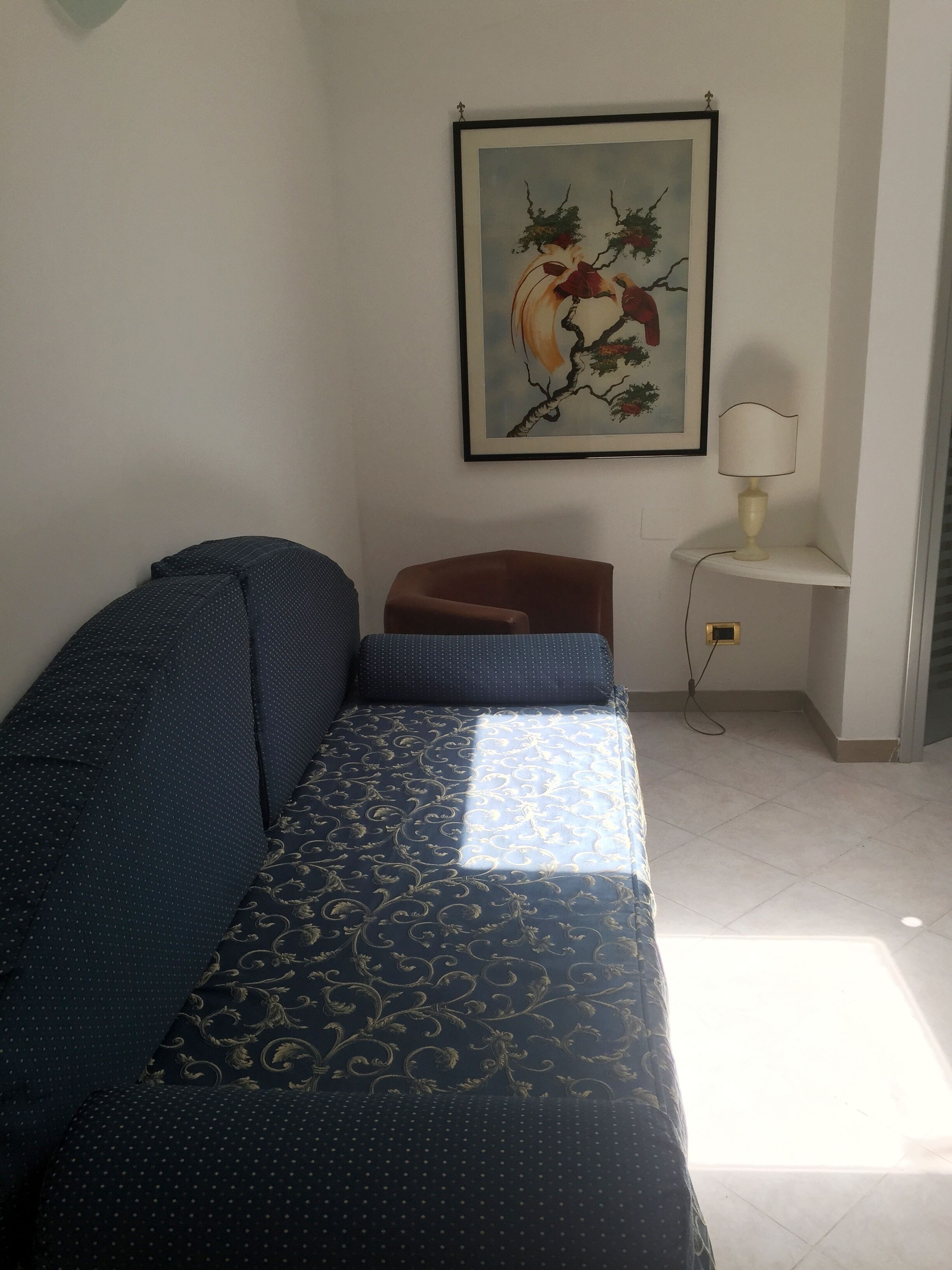 Una habitación con cama, una silla, una lámpara y un cuadro en la pared.