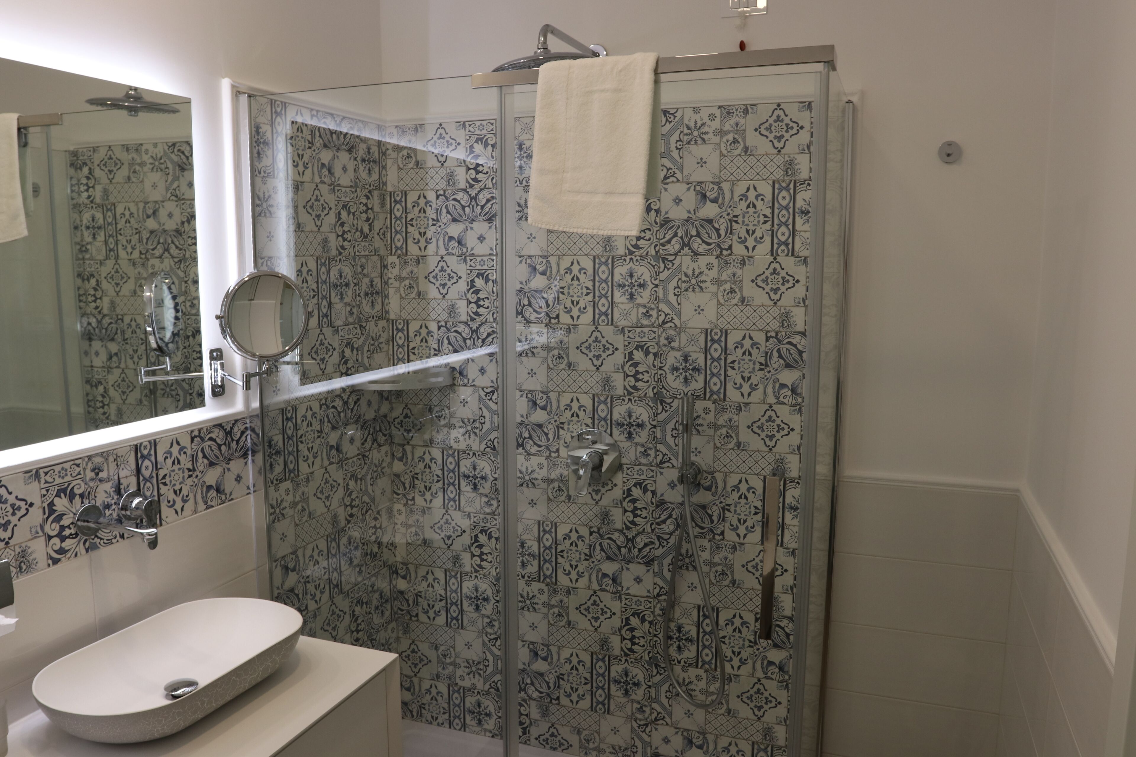 A bathroom with a glass-enclosed shower, a sink with a mirror, and patterned tiles.