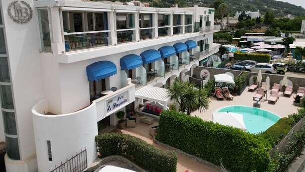 A hotel with a pool, outdoor seating, and a mountain backdrop. - Bougainville Luxury Boutique Hotel (Anacapri)