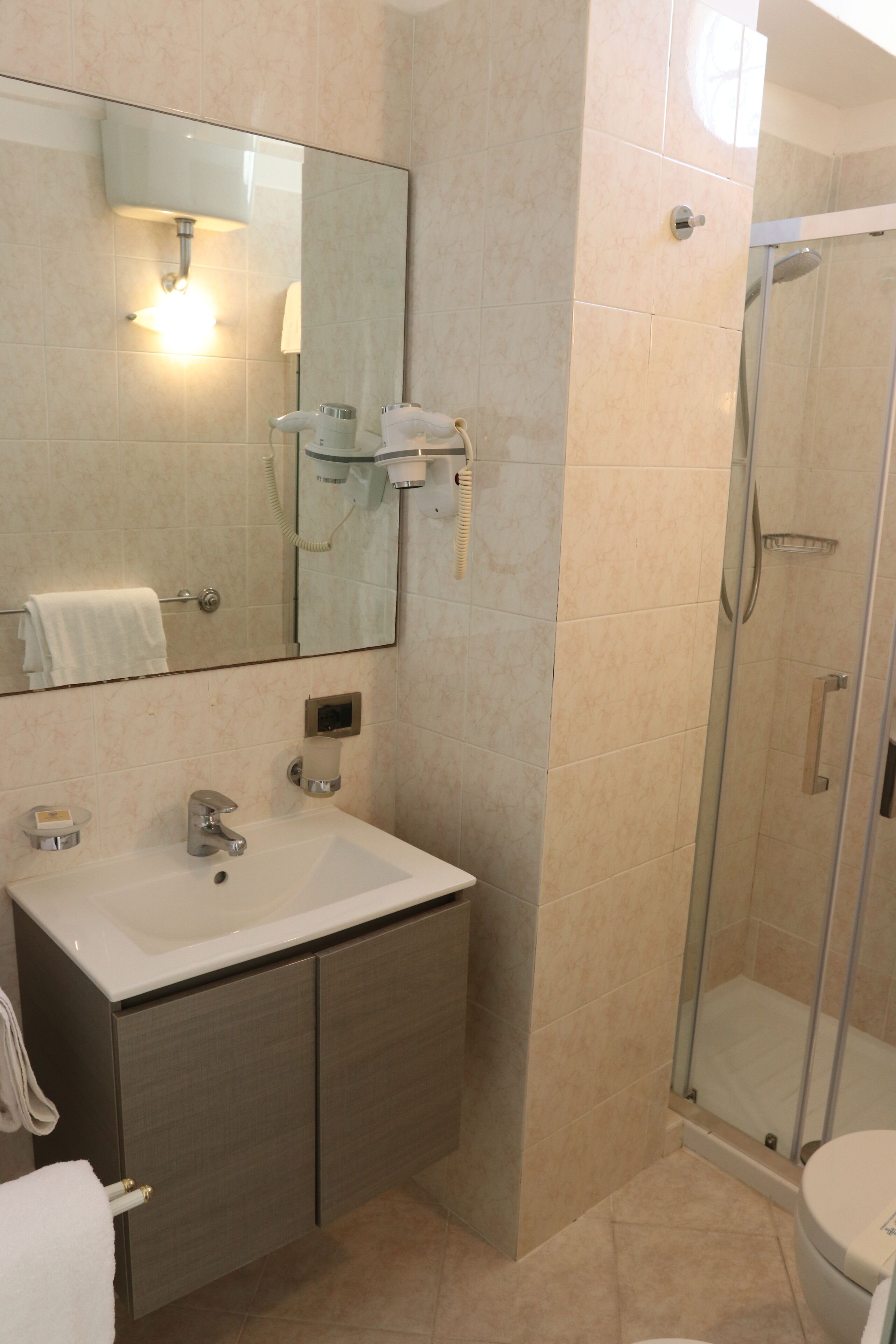 A bathroom with a sink, mirror, towel rack, and a glass-enclosed shower.