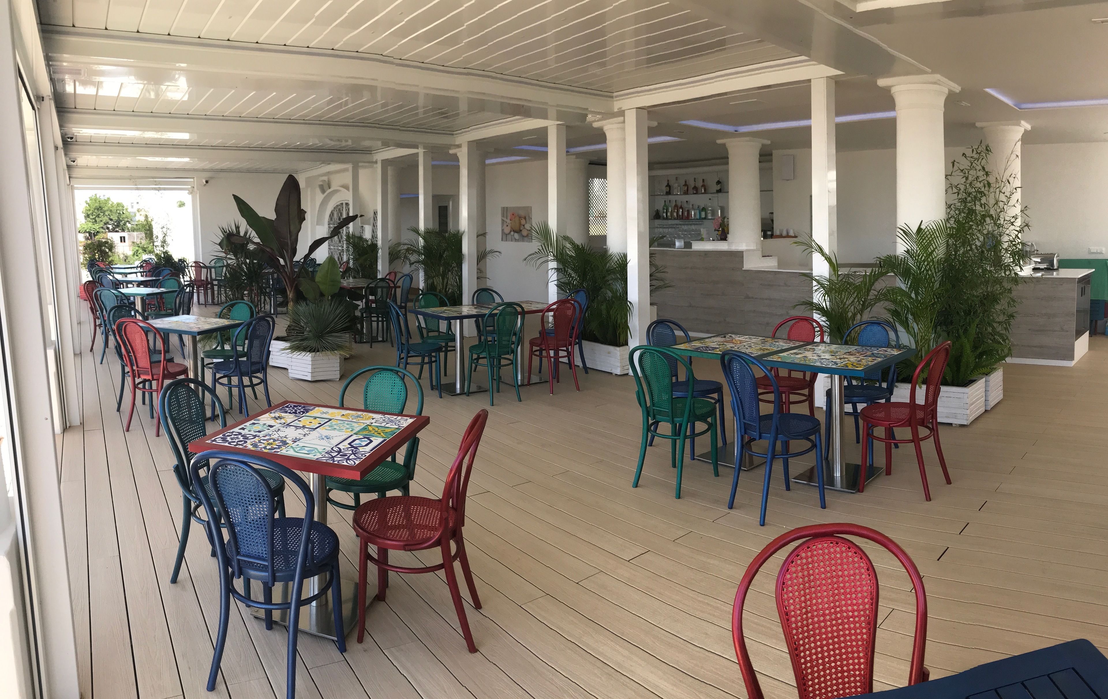 An outdoor patio area with multiple tables and chairs, some with colorful tablecloths.