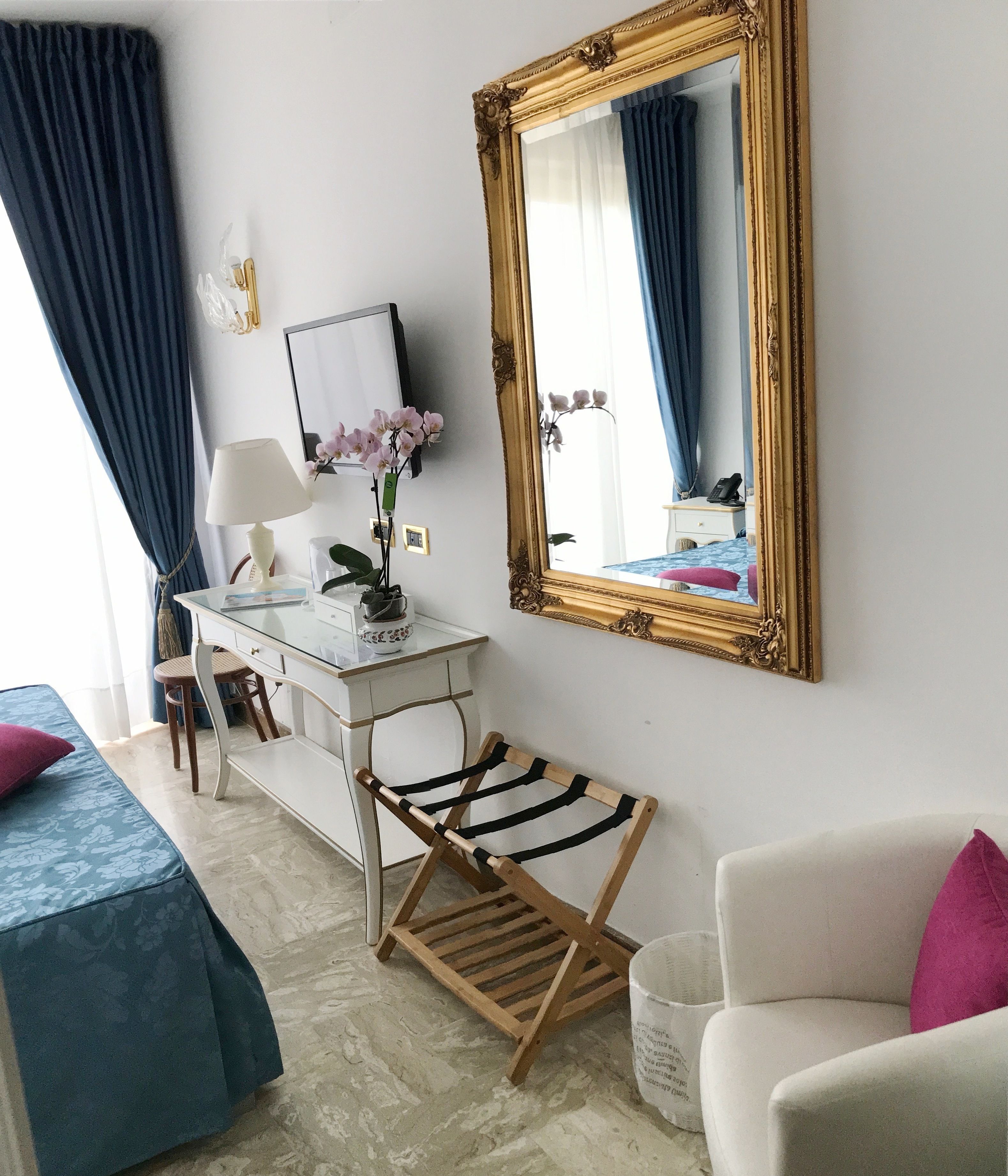 Une chambre d’hôtel avec un lit, un bureau doté d’une lampe, un miroir et un porte-vêtements en bois.