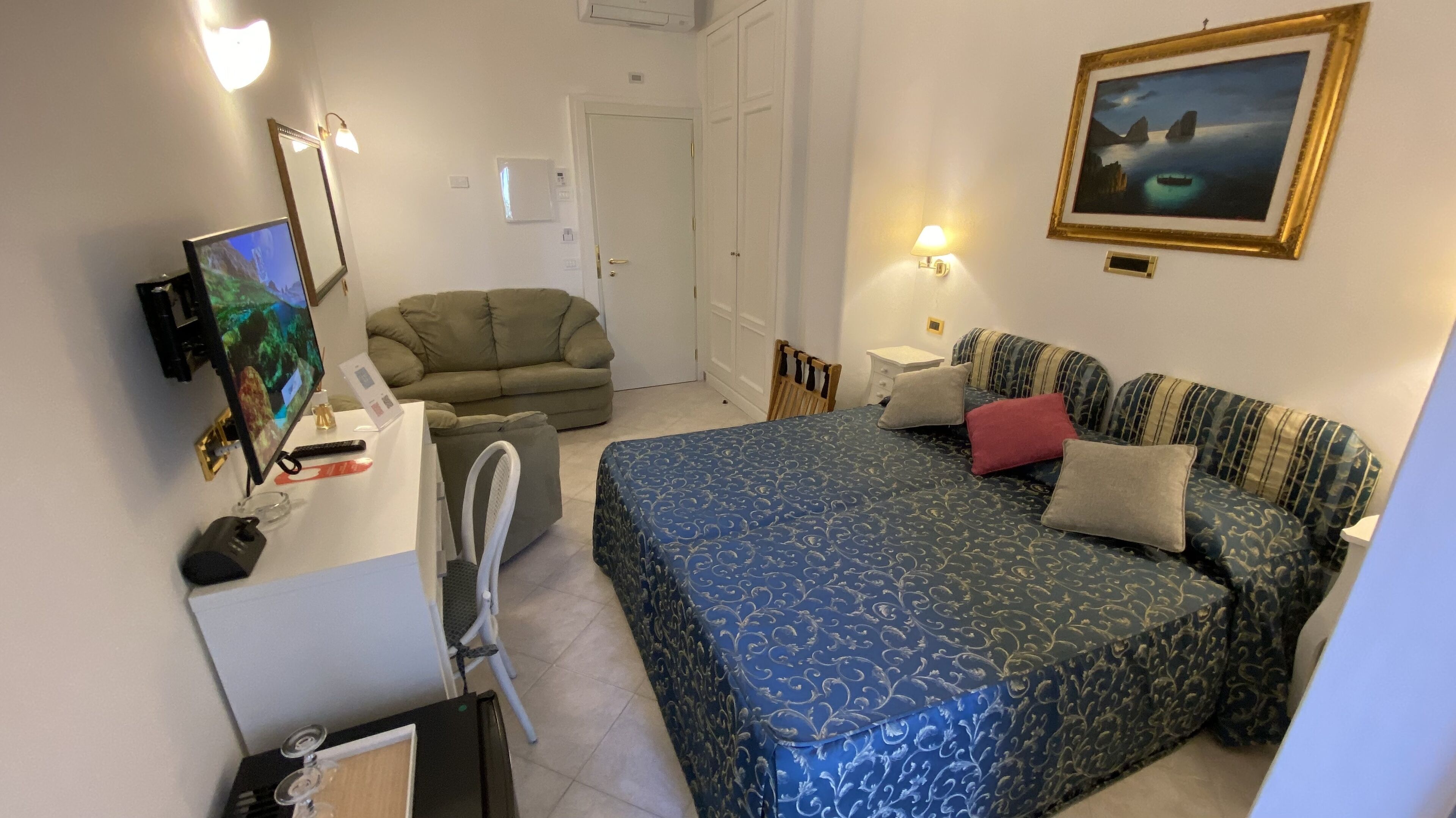 Ett sovrum med en säng, ett skrivbord, en stol, en soffa och en tavla på väggen.