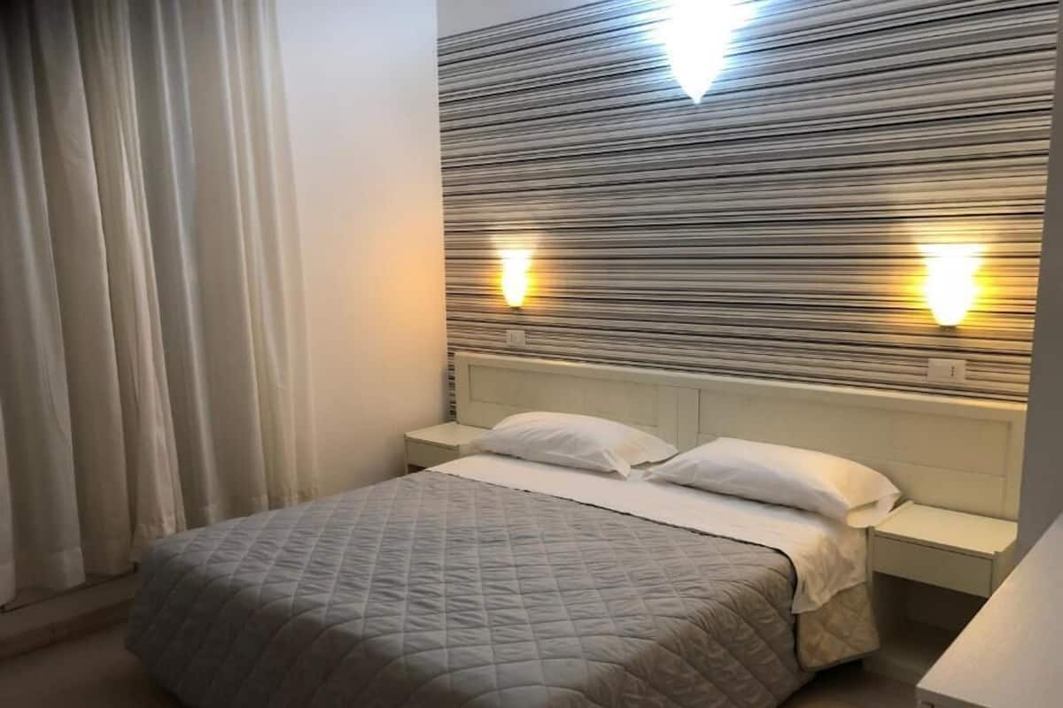 A neatly made bed with a quilted blanket, a bedside table, and a wall-mounted light fixture.