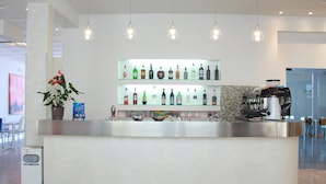 A modern bar area with a stainless steel counter, shelves of liquor bottles, and a coffee machine.