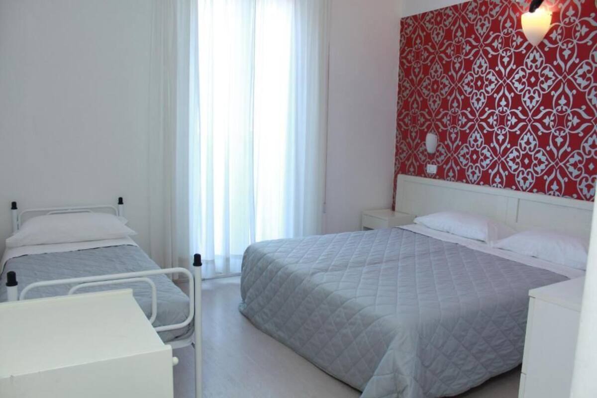 A hotel room with two beds, a bedside table, a nightstand, and a red patterned wall.