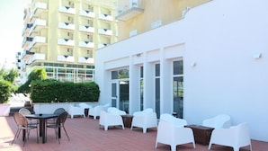 An outdoor patio with white chairs and tables, a building with large windows, and a yellow building in the background.