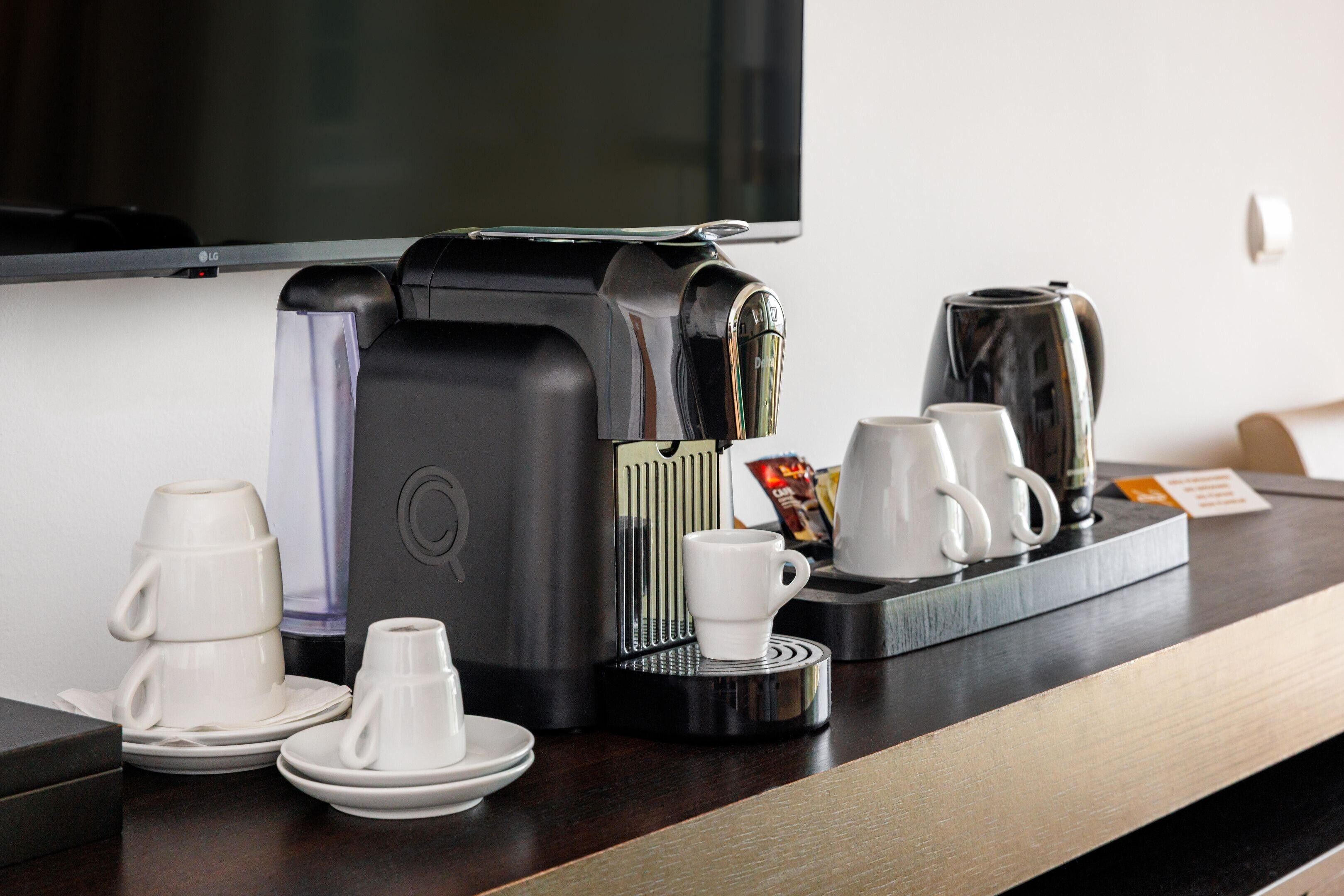 Un coin café avec une machine à café, des tasses et une bouilloire, le tout installé sur un comptoir.