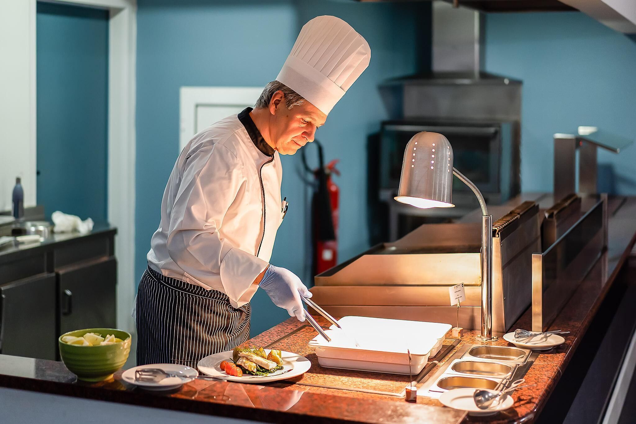 A chef preparing food in a kitchen with a blue wall, stainless steel appliances, and a modern design.