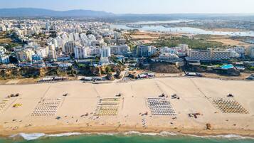 An aerial view of a coastal city with a wide beach, numerous buildings, and a clear view of the sea.
