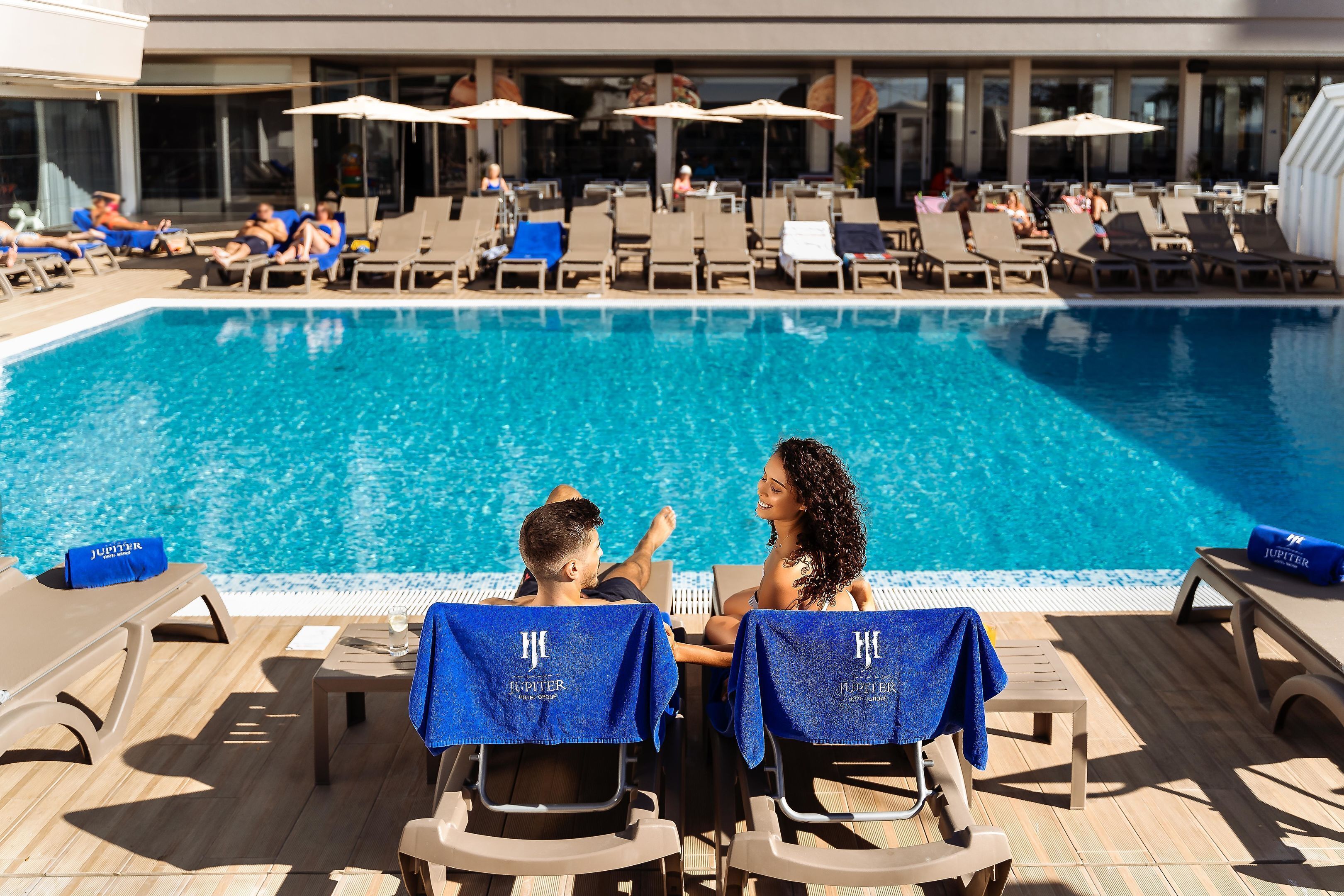 A poolside area with lounge chairs and umbrellas, a pool, and a building in the background.