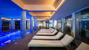 A modern indoor pool area with lounge chairs and a blue-lit ceiling. - Jupiter Algarve Hotel - Beach & Spa (Portimão)