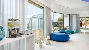A modern hotel lobby with a coffee station, seating area, and large windows offering views of the city. - Jupiter Algarve Hotel - Beach & Spa (Portimão)