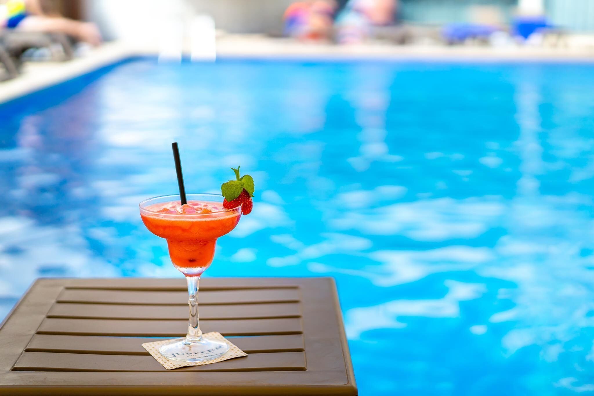 A cocktail on a table by a pool with a blurred background.